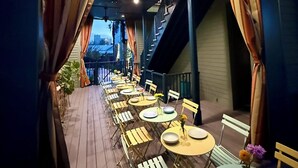 Un espace extérieur aménagé pour les repas, avec des tables et des chaises, une enseigne au-dessus indiquant « Pullman », et un escalier menant à un niveau supérieur.