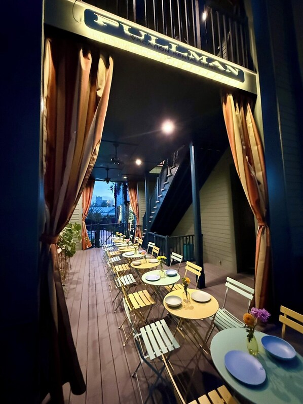 An outdoor dining area with tables and chairs, a sign above reading "Pullman," and a staircase leading to an upper level.