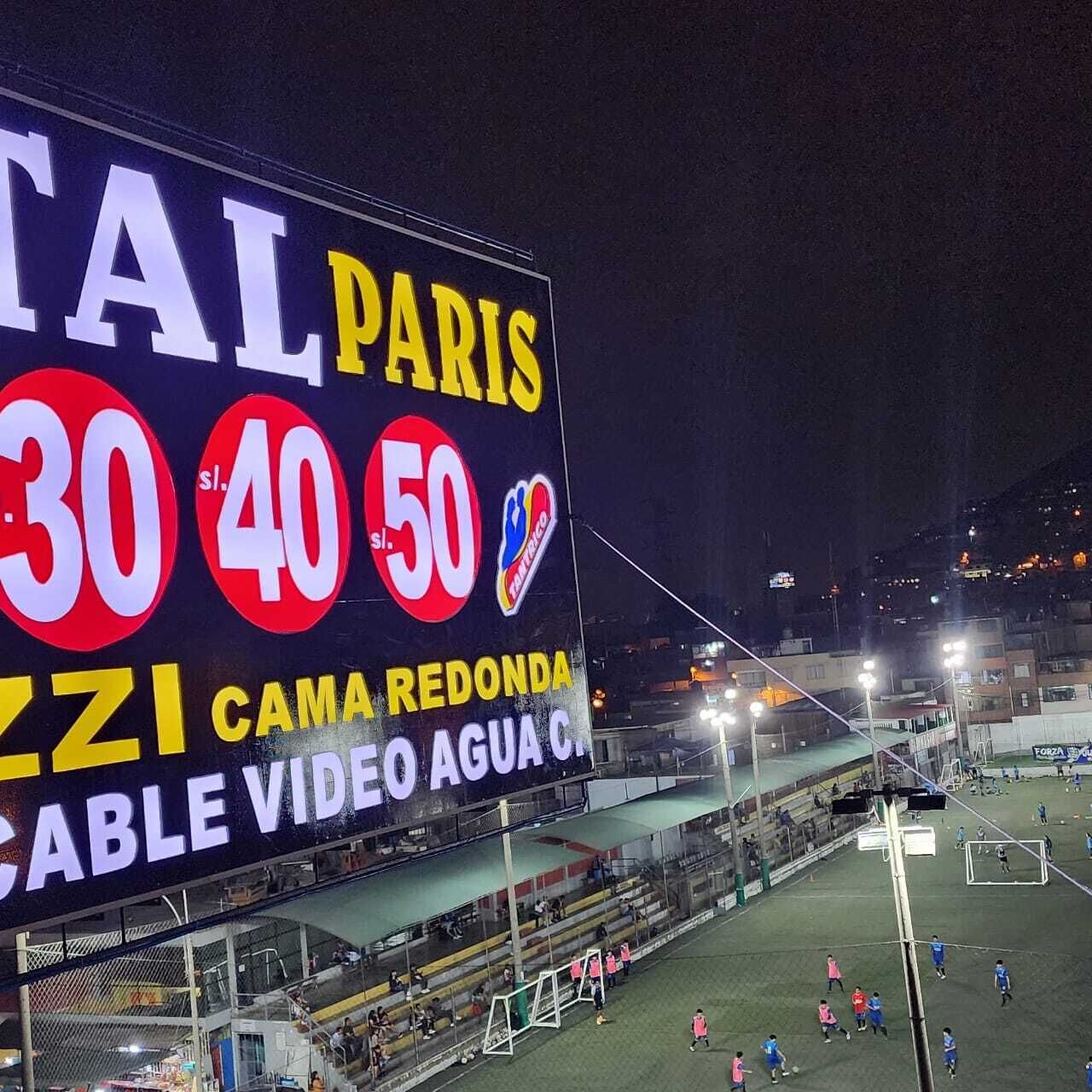 Un estadio deportivo con un marcador digital grande que muestra los resultados y un campo de fútbol.