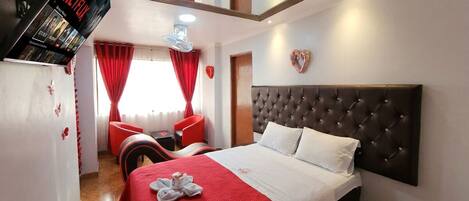Habitación de hotel con cama, televisión montada en la pared, espejo sobre la cama y cortina roja.