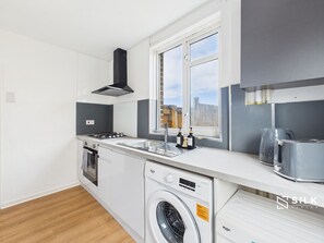 A compact kitchen with a washing machine, a stove, and a window.