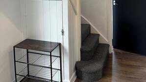 A staircase with a dark door at the top, a small table with a metal frame, and a hanging light fixture. - Modern 3-Bed | Home Near QA Hospital | Sleeps 7 (Cosham)