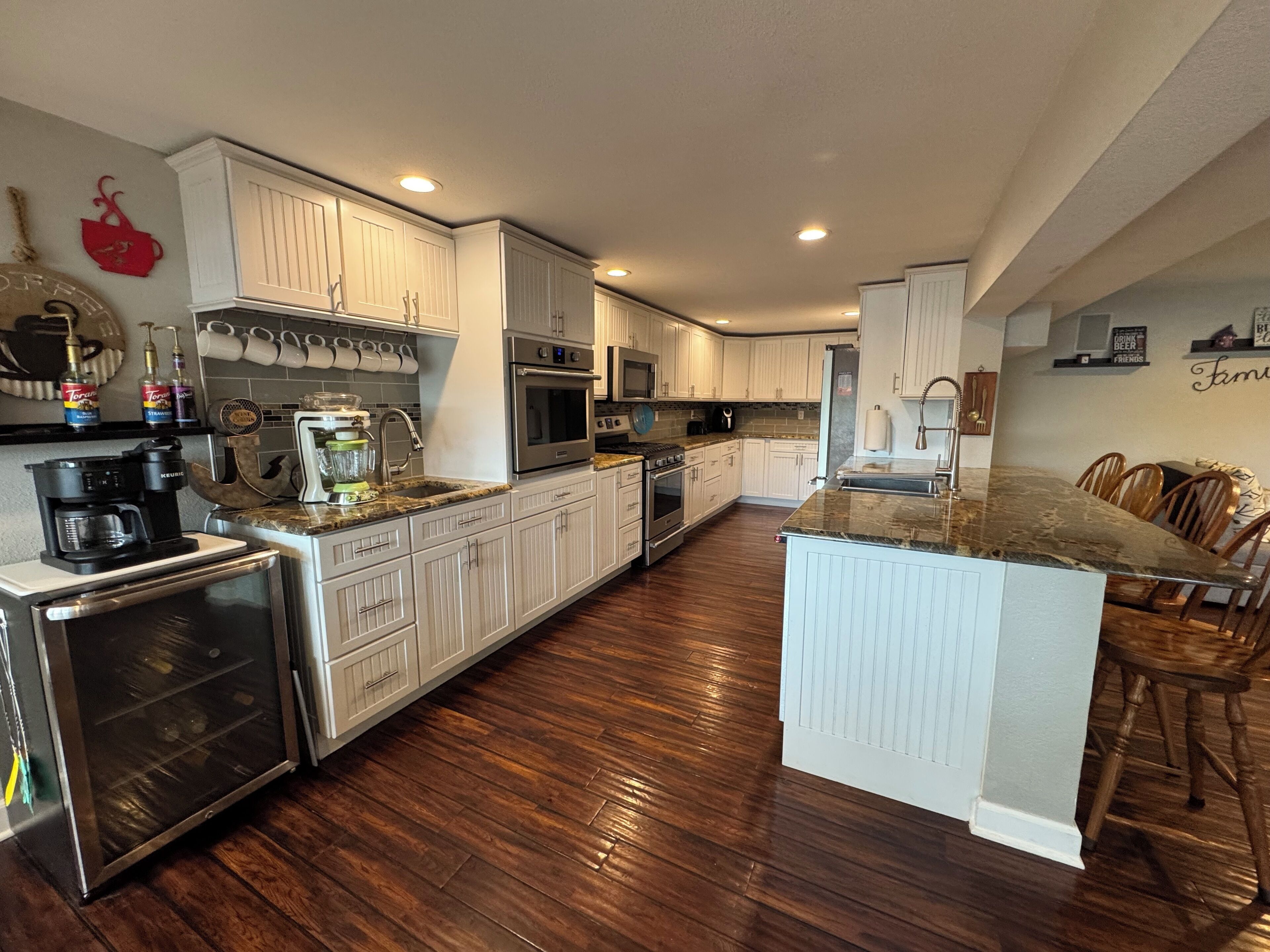 Une cuisine moderne avec des meubles blancs, des appareils en acier inoxydable et un plancher en bois.