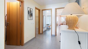 Un couloir avec des portes en bois, une armoire blanche avec une lampe, et un tableau encadré au mur.