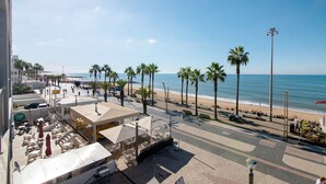 Un hôtel situé en bord de mer, doté d’une terrasse, de palmiers et offrant une vue sur l’océan.