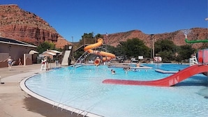 A swimming pool with a water slide and a red slide, surrounded by a mountainous landscape.