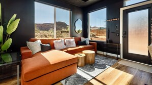 A modern living room with a sectional sofa, large windows, a mirror, and a view of the desert.