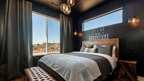A bedroom with a large bed, a bench, and a view of the desert.