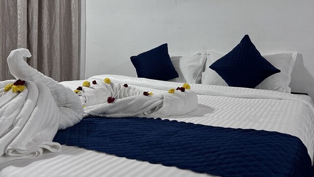 Un lit bien fait, recouvert d’une couette blanche et bleue, avec deux oreillers bleu foncé et une serviette à motifs floraux.