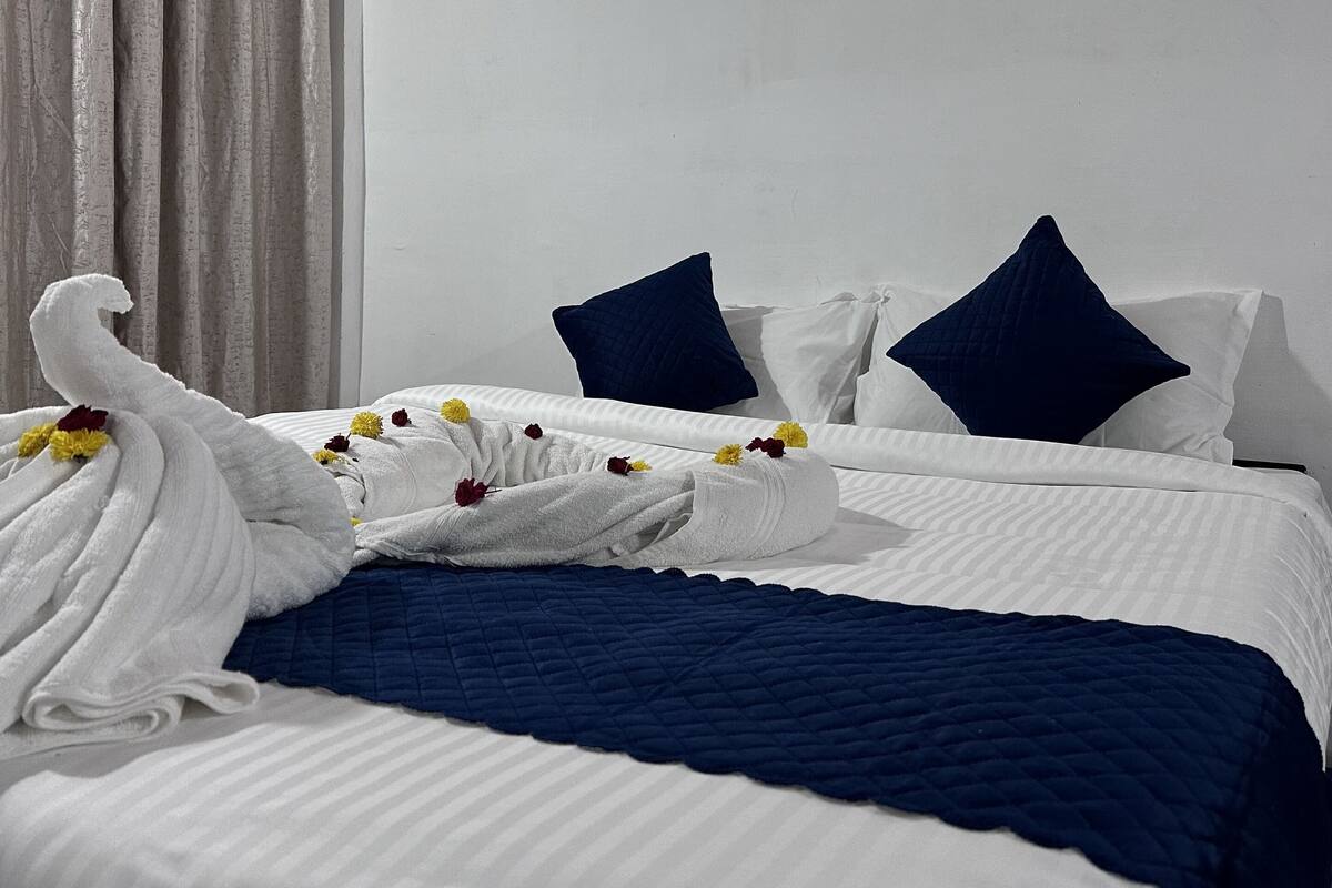 Un lit bien fait, recouvert d’une couette blanche et bleue, avec deux oreillers bleu foncé et une serviette à motifs floraux.