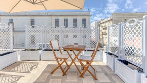 Un espace extérieur aménagé avec une table et des chaises, un grand parasol et une clôture en treillis blanche.