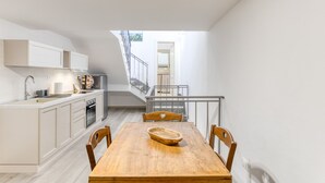 Une cuisine moderne avec des meubles blancs, une table à manger en bois et un escalier menant à l’étage supérieur.