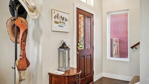 Un pasillo con una puerta de madera, una ventana con persianas y un perchero de pared con sombreros y un farol.