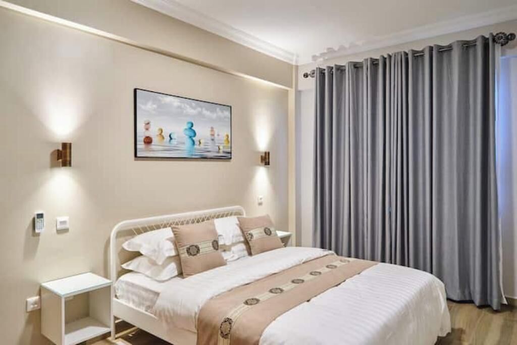 A hotel room with a bed, bedside tables, a painting on the wall, and a window with curtains.