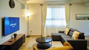 A modern living room with a flat-screen TV, a round coffee table, a sofa, and a yellow armchair.