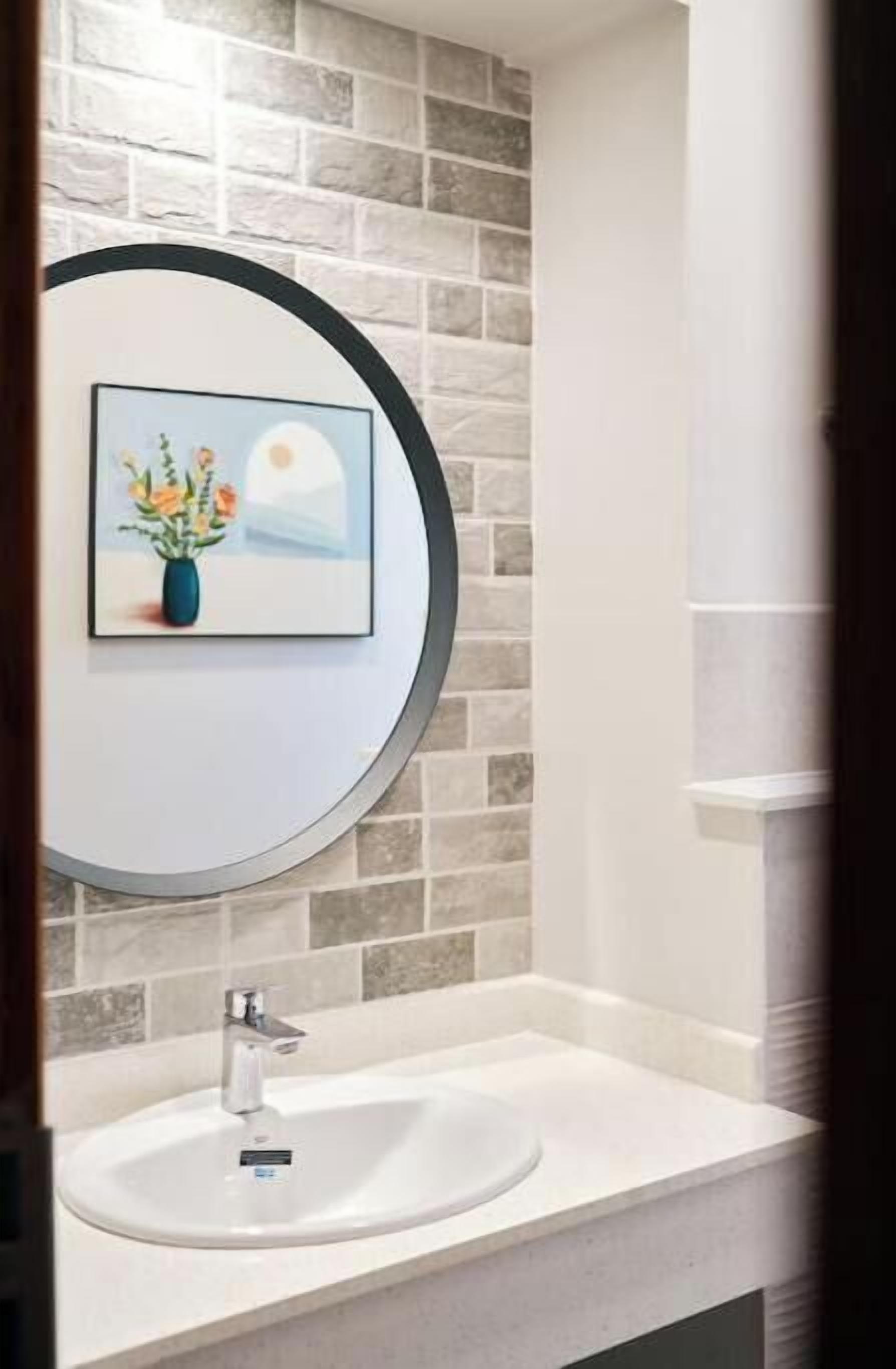 Un bagno con un lavandino bianco, uno specchio rotondo e un quadro con fiori appeso al muro.
