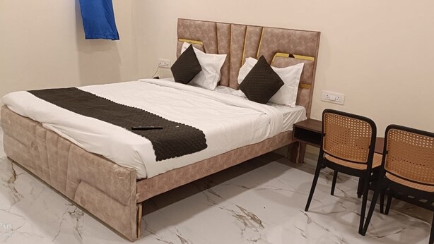 A bed with a headboard, two pillows, a blanket, and a remote control. There are two wicker chairs and a small table. - Hotel BR Palace - Airport Zone (Hyderabad)