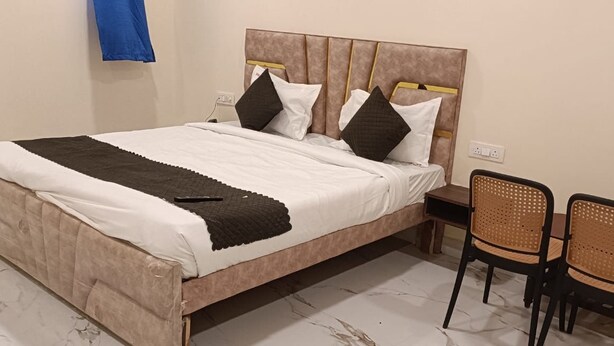 A bed with a headboard, two pillows, a blanket, and a remote control. There are two wicker chairs and a small table. - Hotel BR Palace - Airport Zone (Hyderabad)
