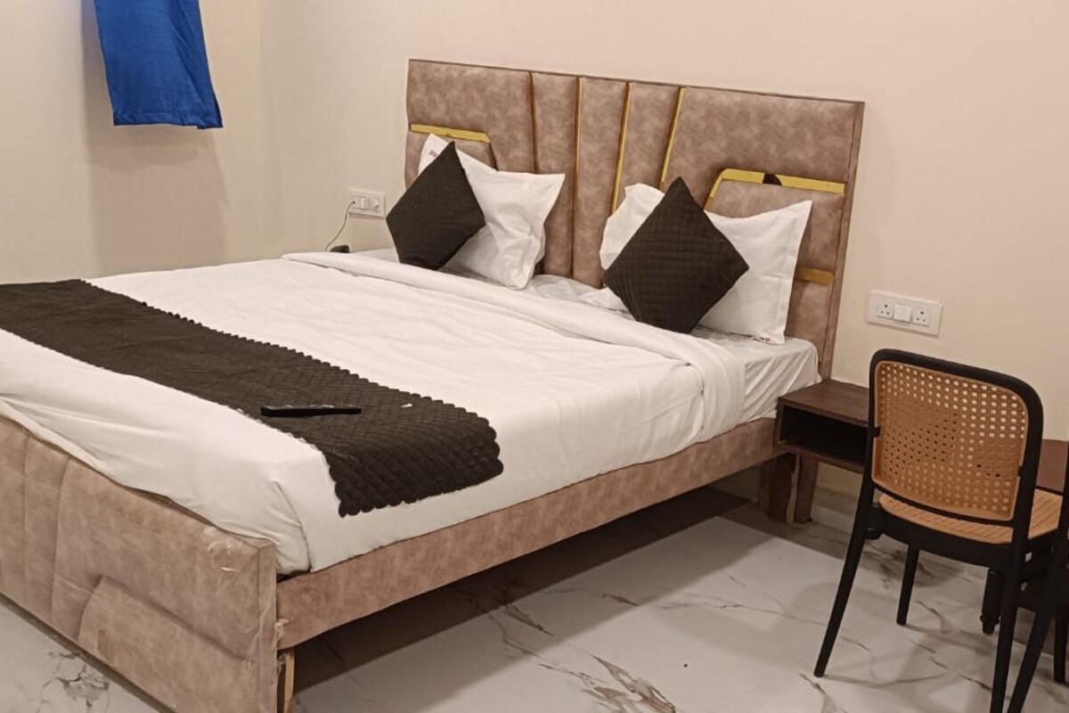A bed with a headboard, two pillows, a blanket, and a remote control. There are two wicker chairs and a small table.