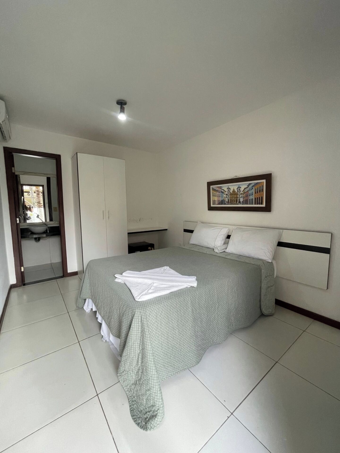 A bedroom with a bed, a wardrobe, a bathroom, and a painting on the wall.