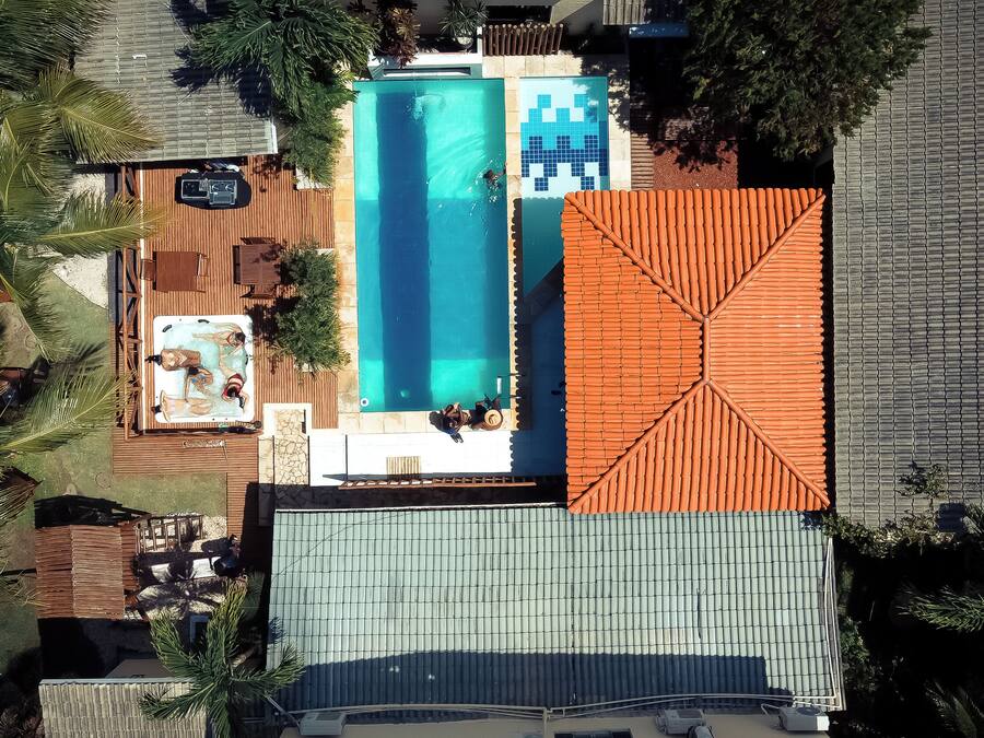 Vista aérea de una propiedad con piscina rectangular, zona de patio techada y estructura de techo anaranjada grande.