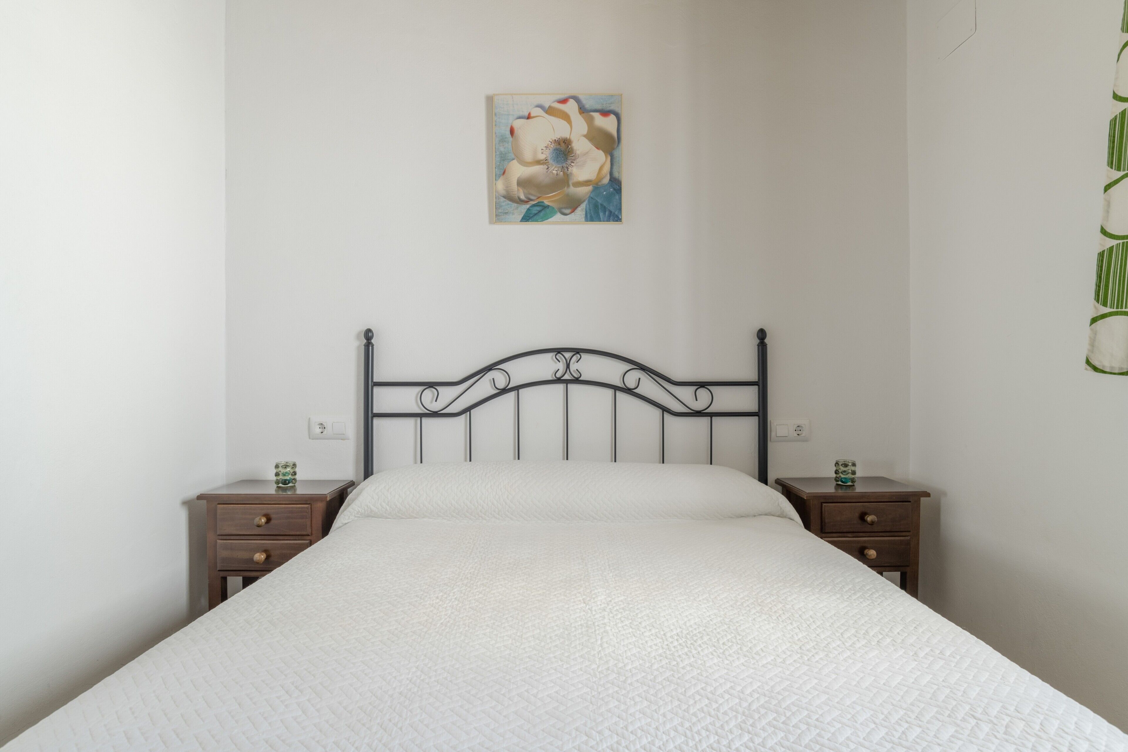 Une chambre à coucher avec un lit, deux tables de chevet, un tableau accroché au mur et une plante verte.
