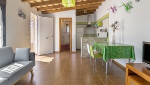 A living room with a sofa, a dining table with chairs, a TV stand, and a kitchen area with a stove and cabinets. - Casa Pepe: Rural Home with Pool & Air Conditioning in Conil (Conil de la Frontera)