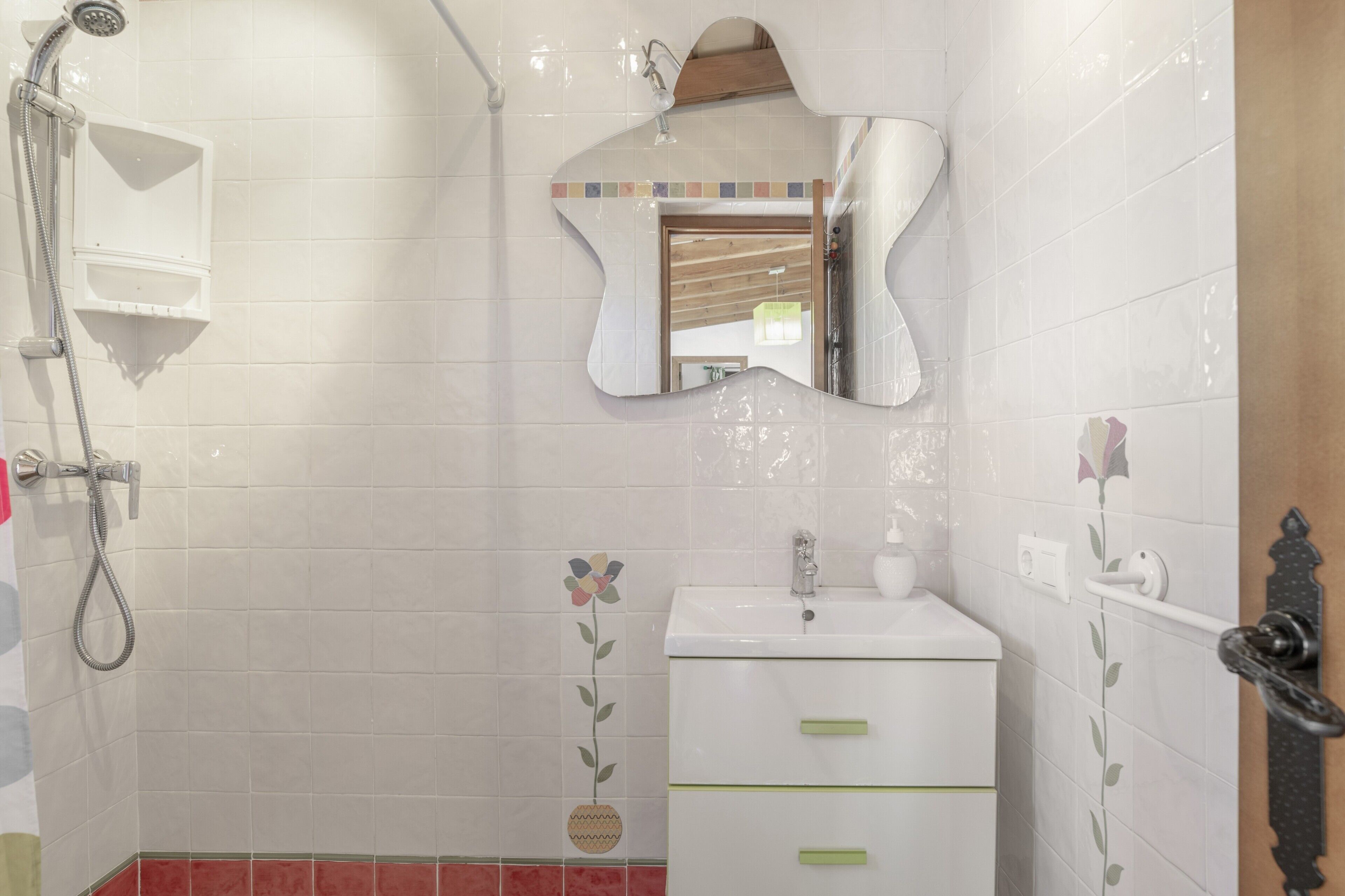 A bathroom with a shower, sink, mirror, and decorative tiles.