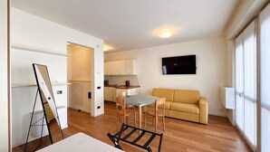 Un espacio habitable compacto con kitchenette, un sofá y un televisor montado en la pared.
