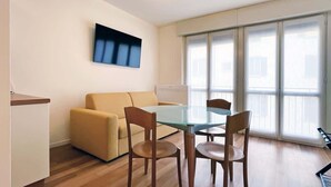 Una sala moderna con un sofá, una mesa de comedor con cubierta de vidrio y dos sillas de madera.