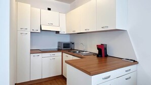 Cocina compacta con armarios blancos, un microondas, un lavabo y una cafetera roja.