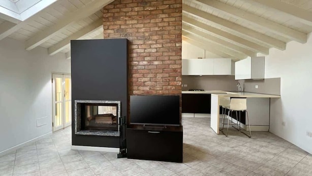 A modern kitchen with a brick wall, a built-in stove, and a dining area with a chair. - Reel House - Affitti Brevi Italia (Lecco)
