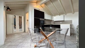 A modern kitchen with a glass dining table and chairs, white cabinets, and a built-in oven. - Reel House - Affitti Brevi Italia (Lecco)