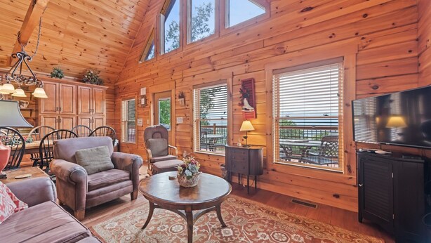 Un acogedor interior de cabaña con paredes de madera, una zona de comedor, una sala de estar con sofá y sillones, una chimenea y un televisor.