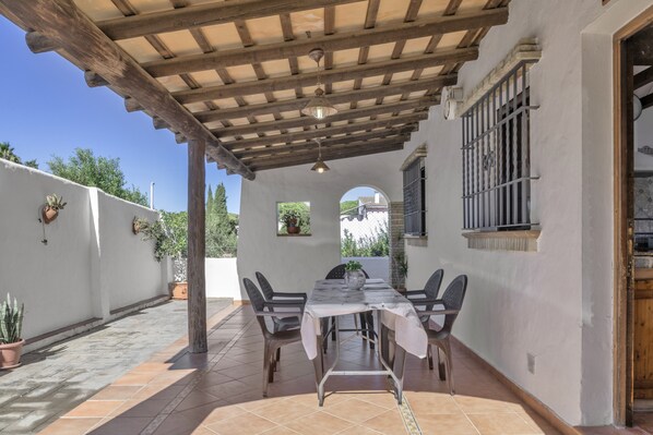 An outdoor patio with a table and chairs, a pergola, and potted plants.
