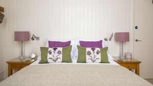 A neatly made bed with floral pillows, two bedside tables with lamps, and a door with a sign. - Scottish Thistle - 1 bedroom with optional sofa bed (Inverness)