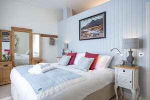 En pænt redt seng med hvide og blå sengetæpper, et indrammet billede af Isle of Skye, og en sengetavlelampe på et natbord.