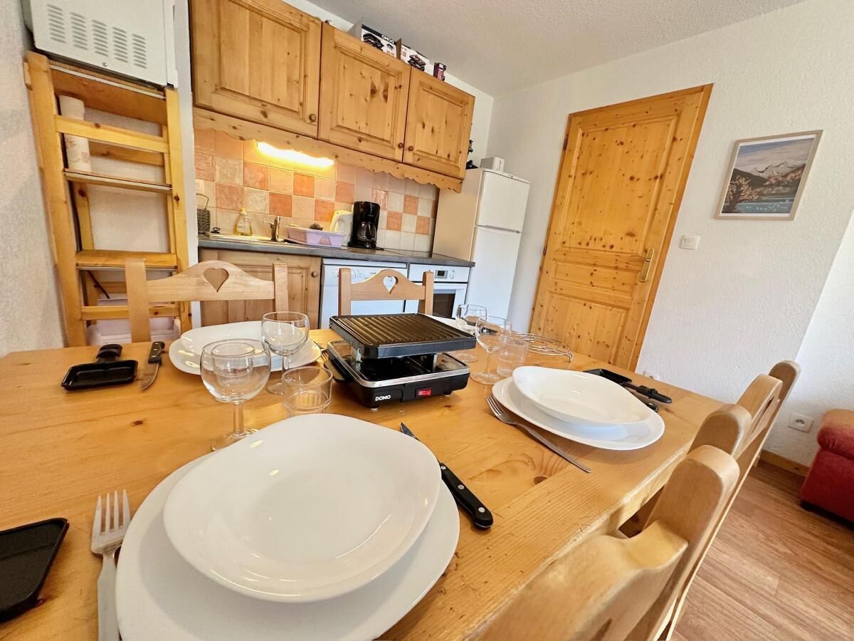 A dining area with a wooden table set for two, a portable grill, and wooden cabinets in the background.