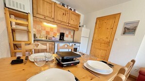 A dining area with a wooden table set for two, a portable grill, and wooden cabinets in the background.