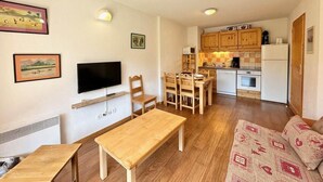 A compact living space with a dining area, a sofa, a TV, and a kitchenette.