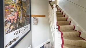 Eine Treppe mit Teppichstufen und roter Umrandung, ein gerahmtes Bild einer Landschaft und ein Korbwägelchen an der Wand.