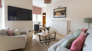 Ein Wohnzimmer mit Flachbildfernseher, einem Holztisch und einer Couch mit gemusterten Kissen.