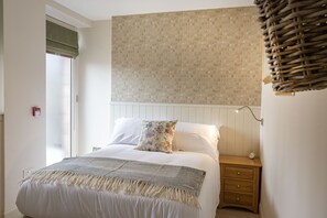A bedroom with a bed, a nightstand, a wall-mounted lamp, and a window with a blind. - The Courtyard - sleeps 2 guests  in 1 bedroom (Inverness)