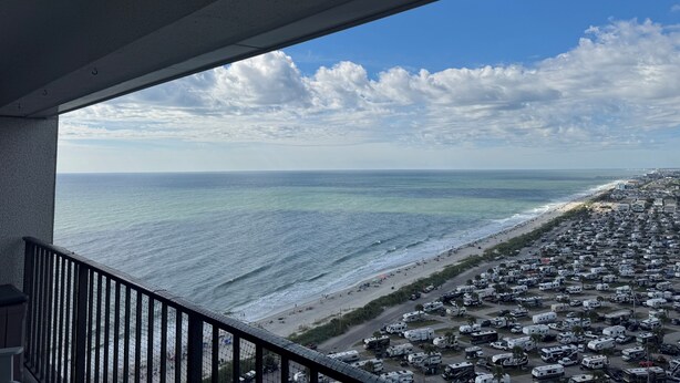 Ein Balkon mit Blick auf das Meer und einen Strand, entlang dessen Ufers Wohnmobile geparkt sind.