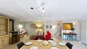 Un coin repas avec une table en bois dressée pour quatre personnes, une chaise rouge et un espace cuisine équipé d’une cuisinière et d’étagères.