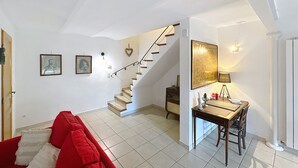Un grand espace de vie comprenant un escalier, une table à manger avec des chaises et un canapé agrémenté de coussins rouges.