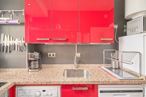 A kitchen with red cabinets, a coffee maker, a sink, and a dish rack.