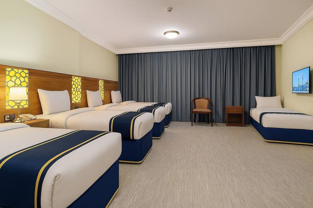 A hotel room with four beds, a wooden headboard, a desk, a chair, and a painting on the wall.