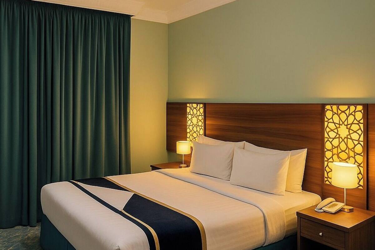 A hotel room with a large bed, two bedside tables with lamps, a headboard with a decorative panel, and a ceiling light.