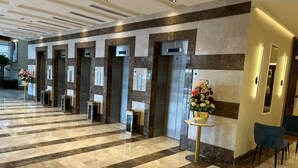 A hotel lobby with a marble floor, elevators, and a reception desk with a vase of flowers. - Al Hashmeih Tower Hotel Makkah (Makkah)